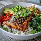 Golden-brown soy ginger salmon fillets glazed in sauce, nestled on steamed rice with crisp vegetables and sliced avocado.