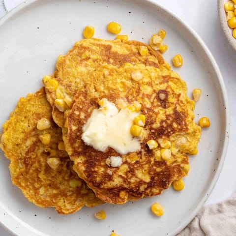 A stack of freshly-cooked Corn Flapjacks, slightly crisp edges, served with a drizzle of maple syrup.