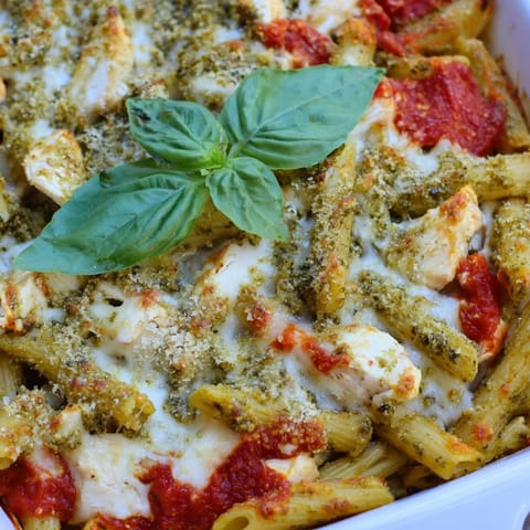 A slice of Pesto Chicken Pasta Bake shows tender chicken, penne, and vibrant green pesto mixed in.