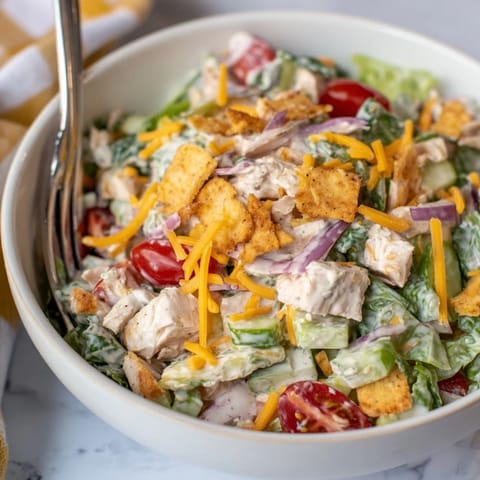 A close-up of creamy jalapeño ranch dressing drizzled over chopped chicken, cucumbers, and red onion in a salad.  