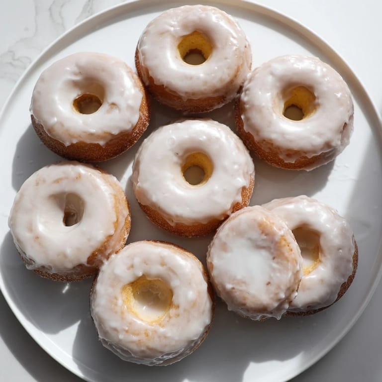 A close-up of golden brown muffin tin donuts, glistening under a sweet, vanilla-infused glaze.