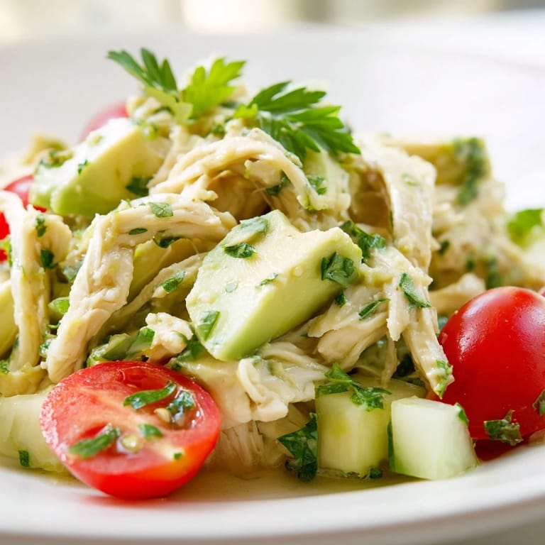 A close-up view of creamy avocado chicken salad with crisp cucumber, red onion, and cilantro on a rustic platter.