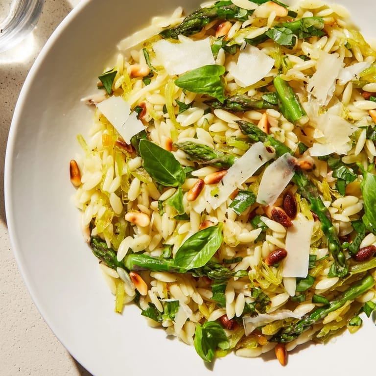 A close-up of vibrant Asparagus Lemon Orzo Salad with toasted pine nuts and baby arugula, ready to serve as a refreshing vegetarian Mediterranean side.