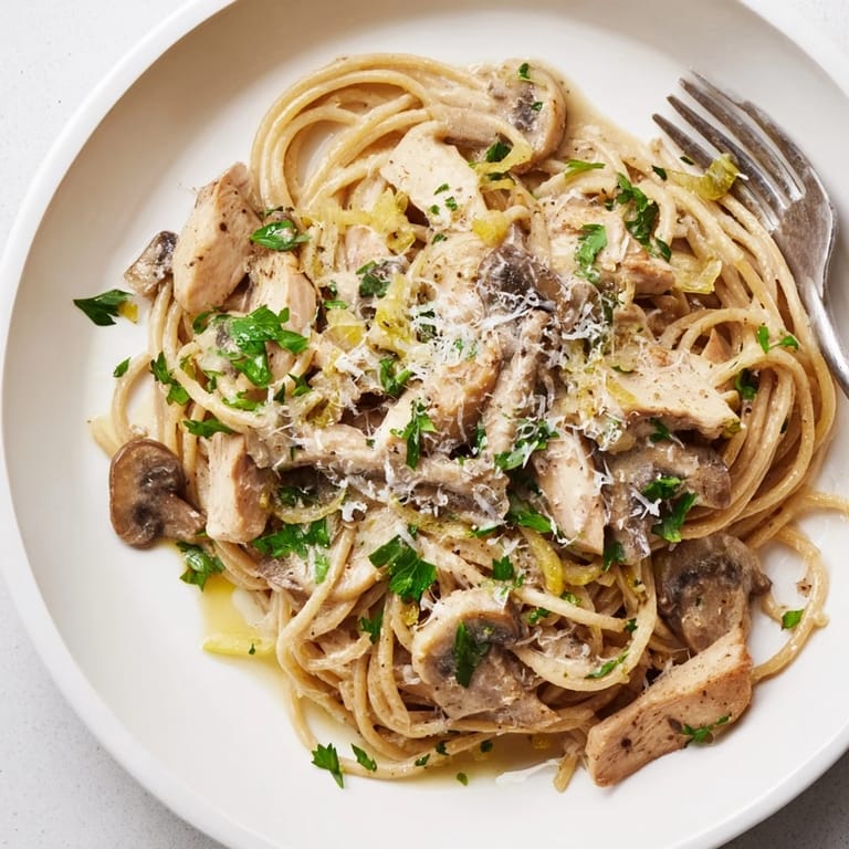 Golden chicken and sautéed mushrooms rest atop a bowl of Creamy Mushroom Chicken Spaghettini, with steam rising from the light Parmesan cream sauce.  
