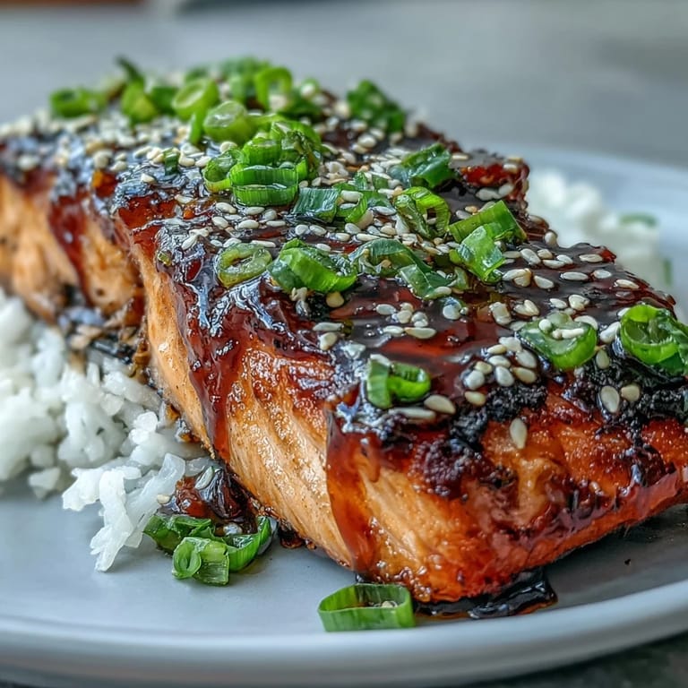 Juicy Maple Soy Glazed Salmon on rice, garnished with sesame seeds and fresh green onions.