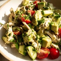 Bright green avocado chunks mingle with shredded chicken, halved cherry tomatoes, and fresh herbs in a creamy lime-dressed salad.
